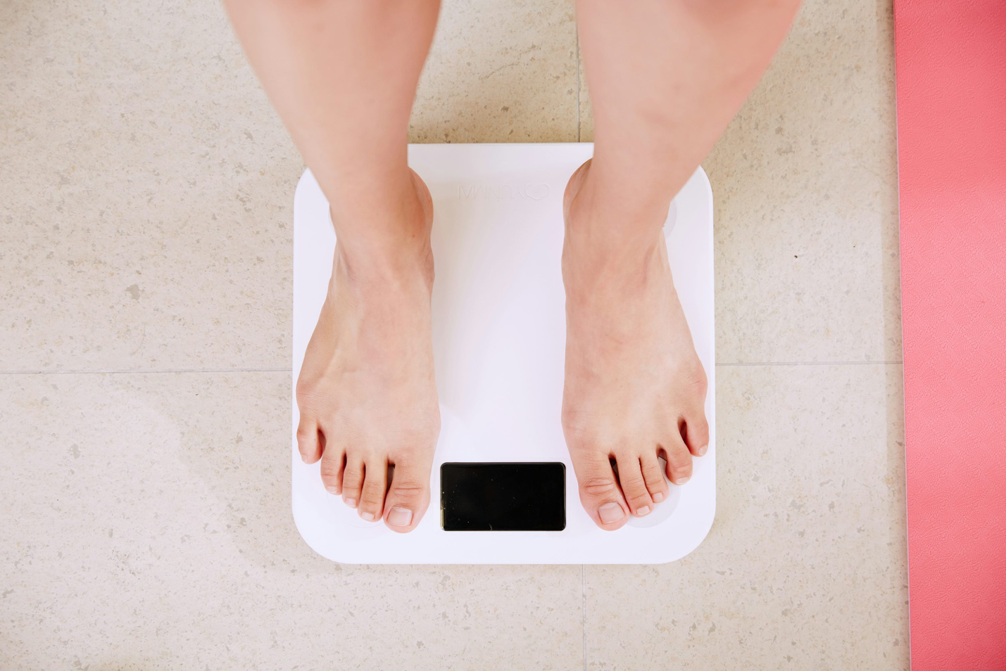 A person standing on a white digital bathroom scale, checking their weight.