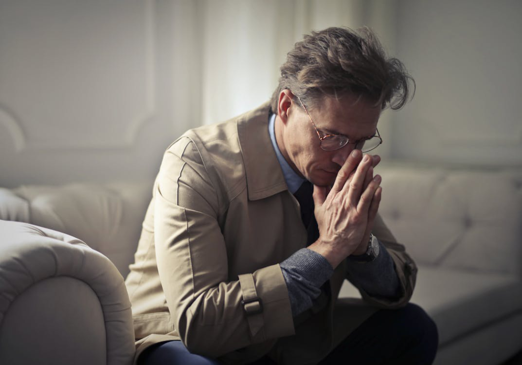 Mature man sitting on a couch looking tired and deep in thought, showing signs of low testosterone.