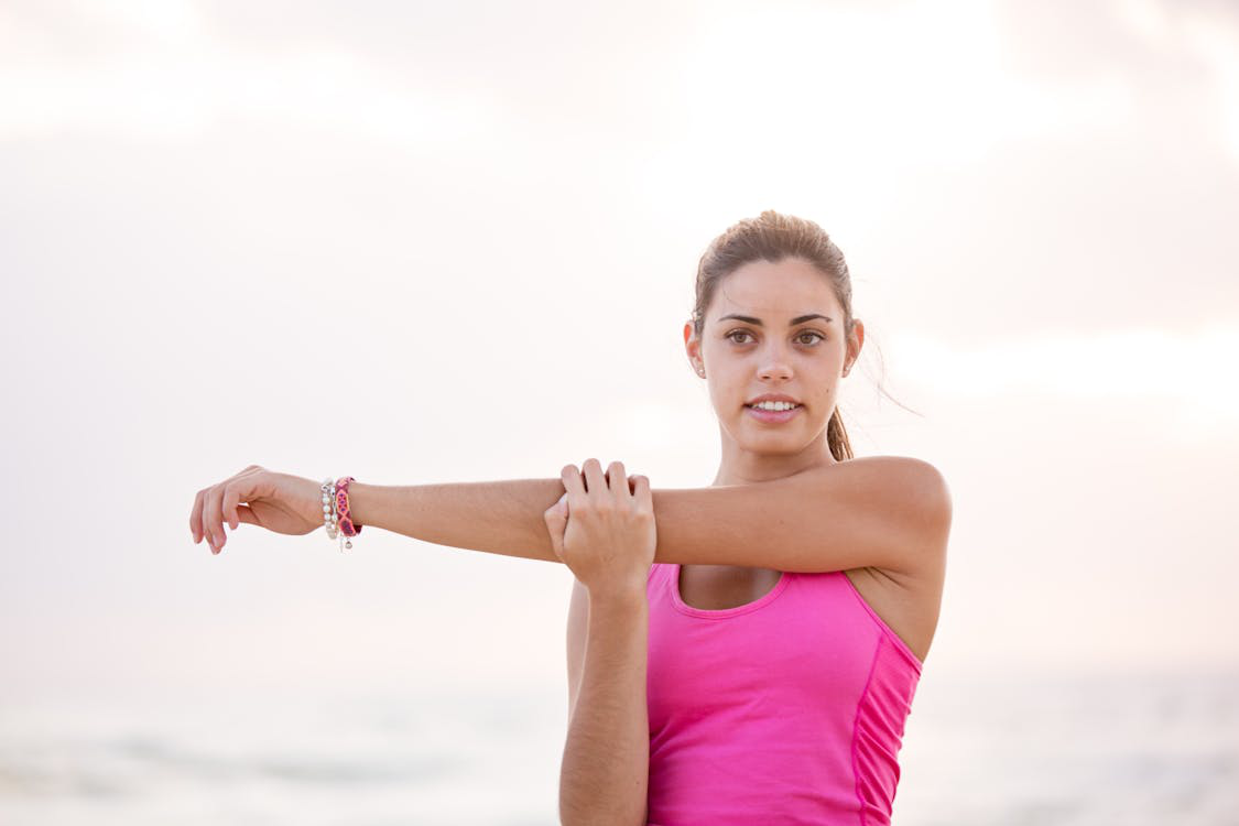 Woman in a pink tank top stretching her arm outdoors