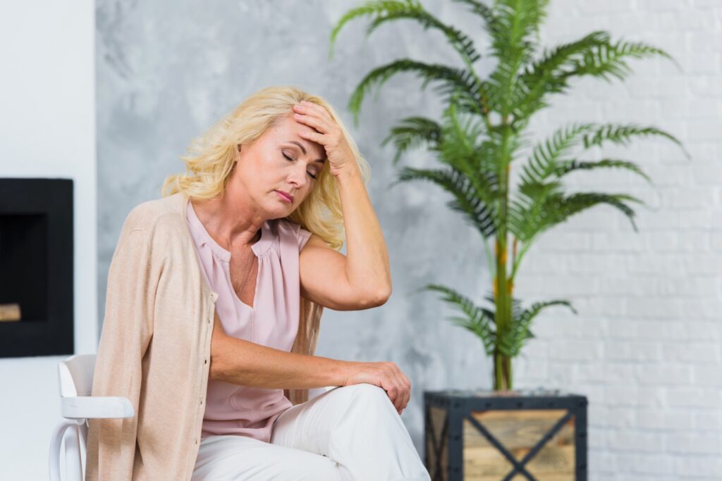 Older woman holding her head with a pained expression, experiencing a menopause-related headache